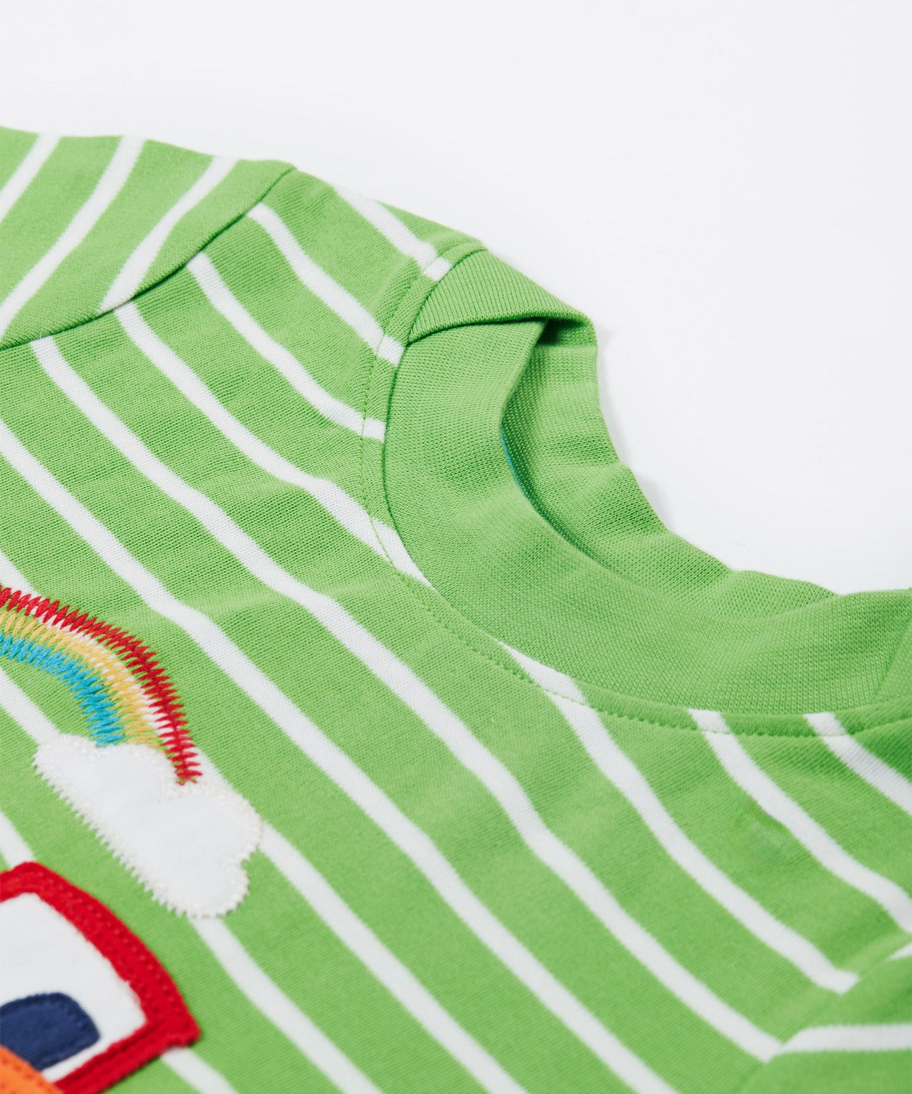 A close up of the Frugi kids breton easy on tractor jumper. Showing the green neck trim and the top part of the red tractor applique and a rainbow embroidery on green and white stripe organic cotton fabric