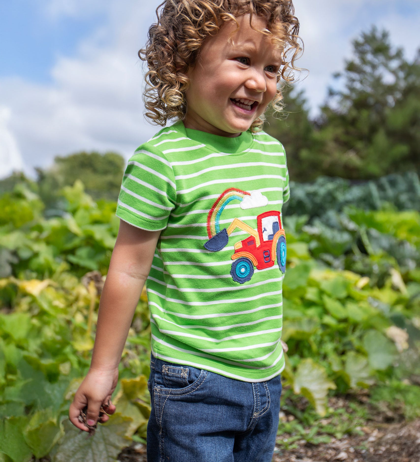 A child wearing a Frugi Tractor Applique  Easy On T-Shirt with denim shorts