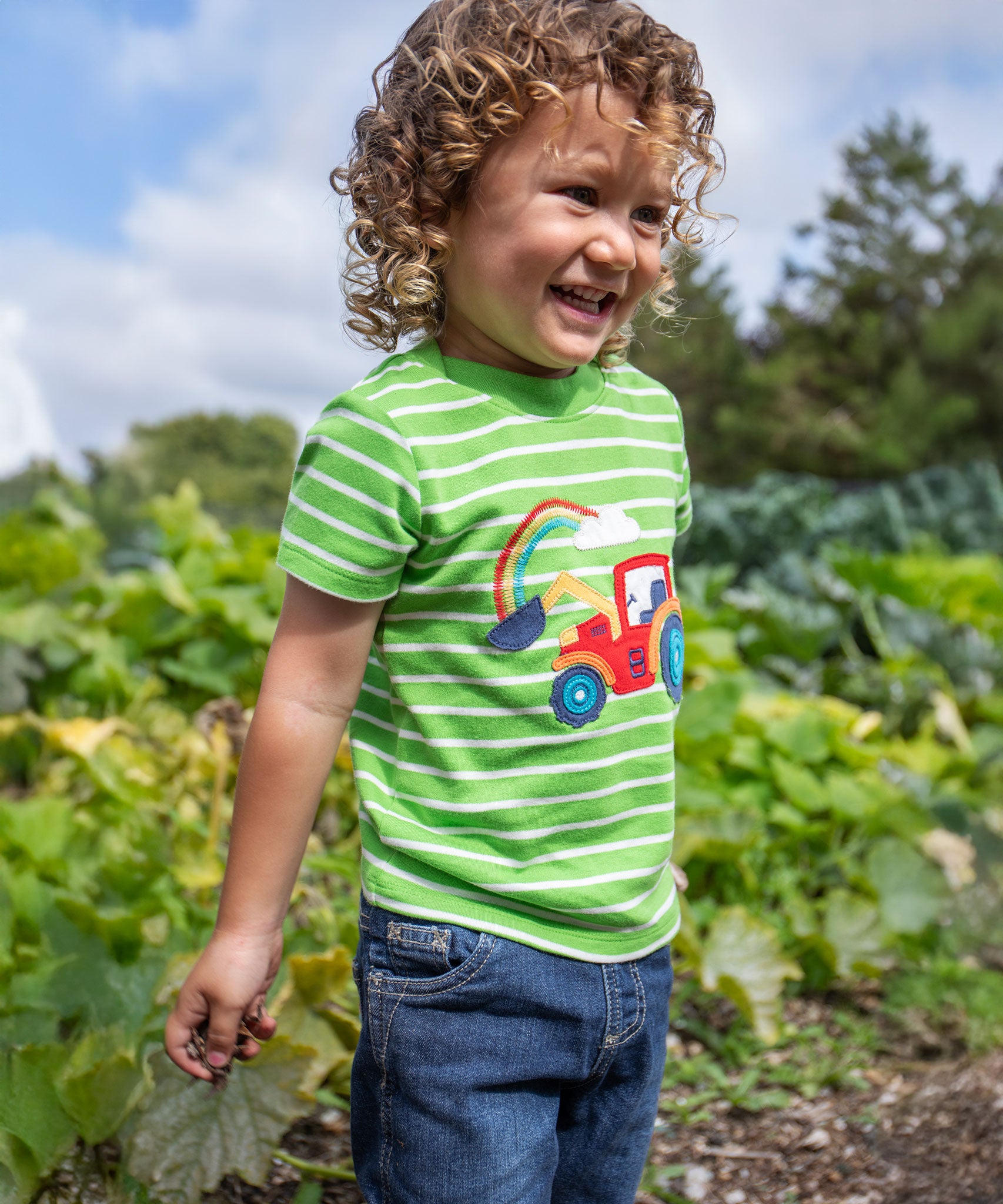 A child wearing a Frugi Tractor Applique  Easy On T-Shirt with denim shorts