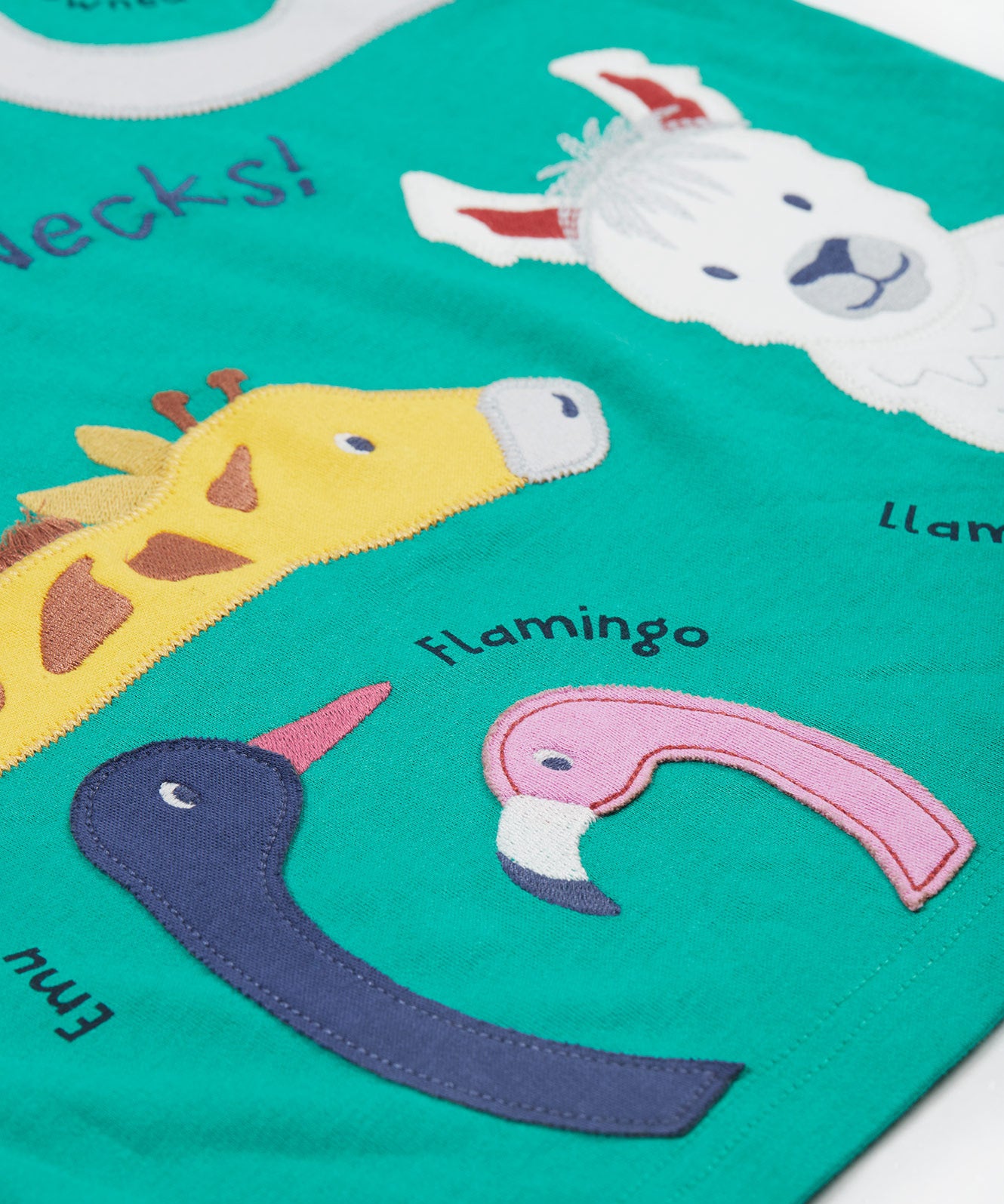 A close up of the Frugi kids long neck pals t-shirt. Showing the different long necked animals appliqué including a giraffe and emu, flamingo and llama with animal names on green organic cotton fabric