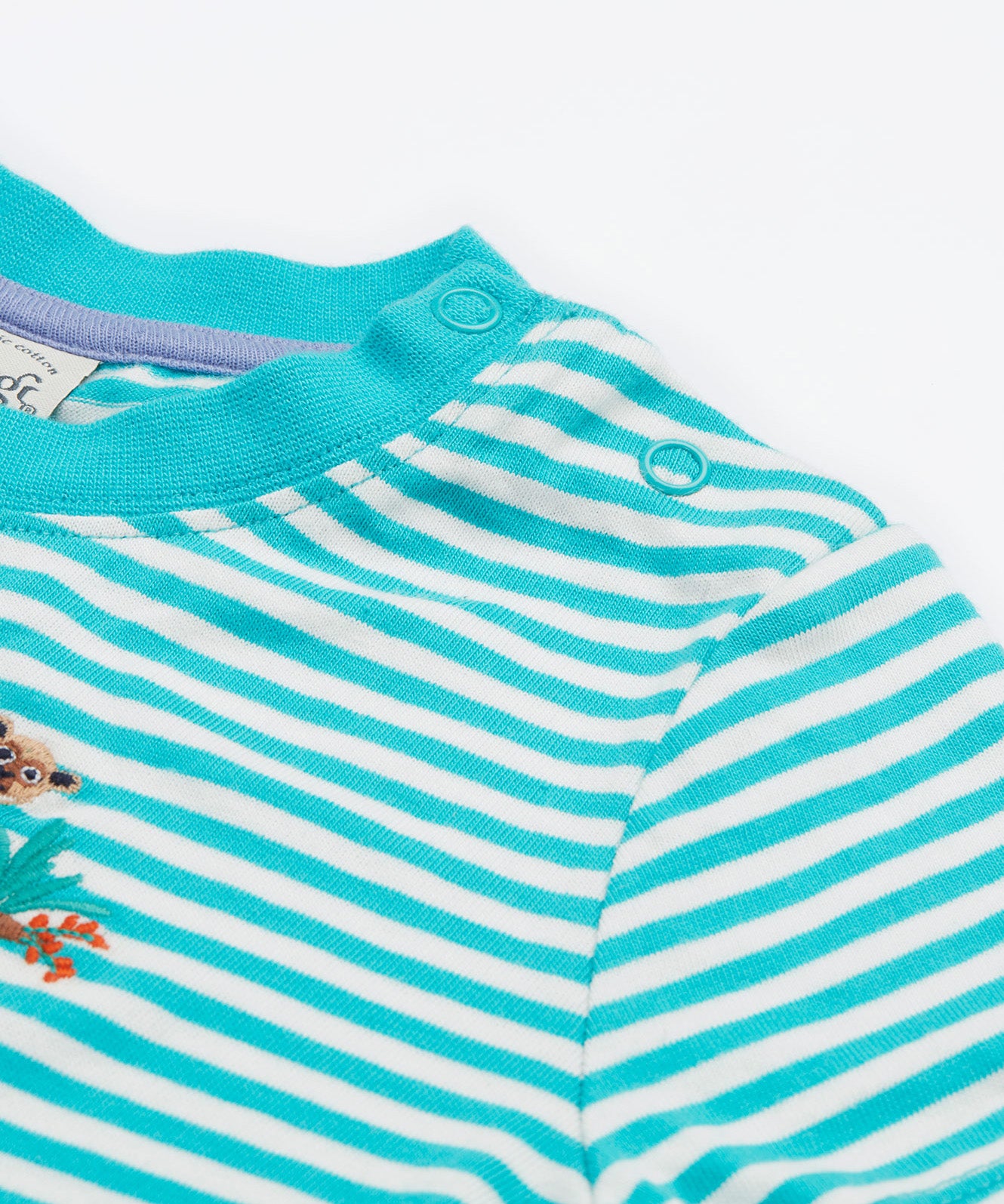 A close up of the Frugi kids moss stripe wildlife t-shirt. Showing the shoulder popper fasteners for easy fitting with a light blue neck trim on a blue and white stripe organic cotton fabric