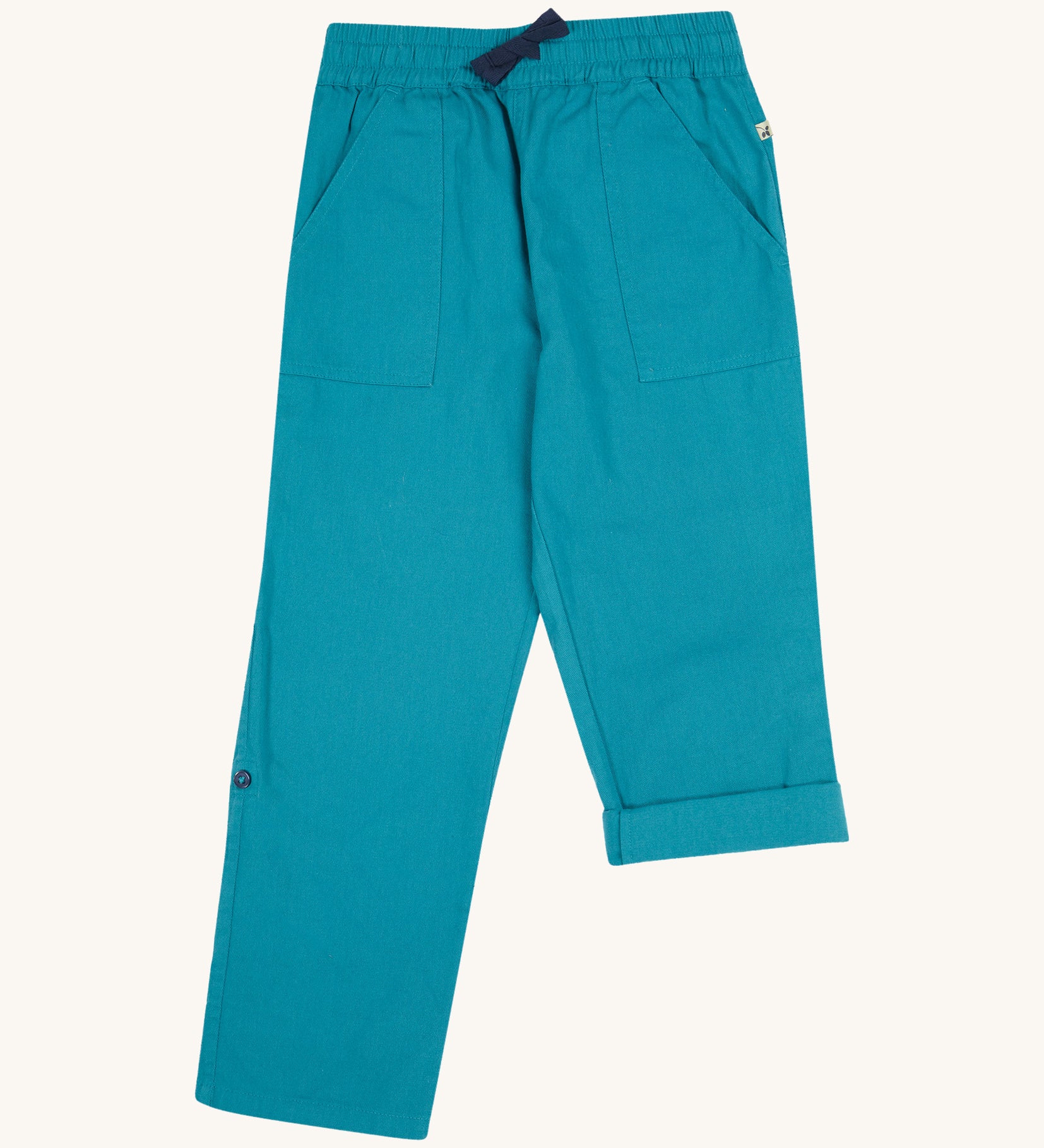 Frugi kids trousers in green, blue, turquoise colour on a cream background.