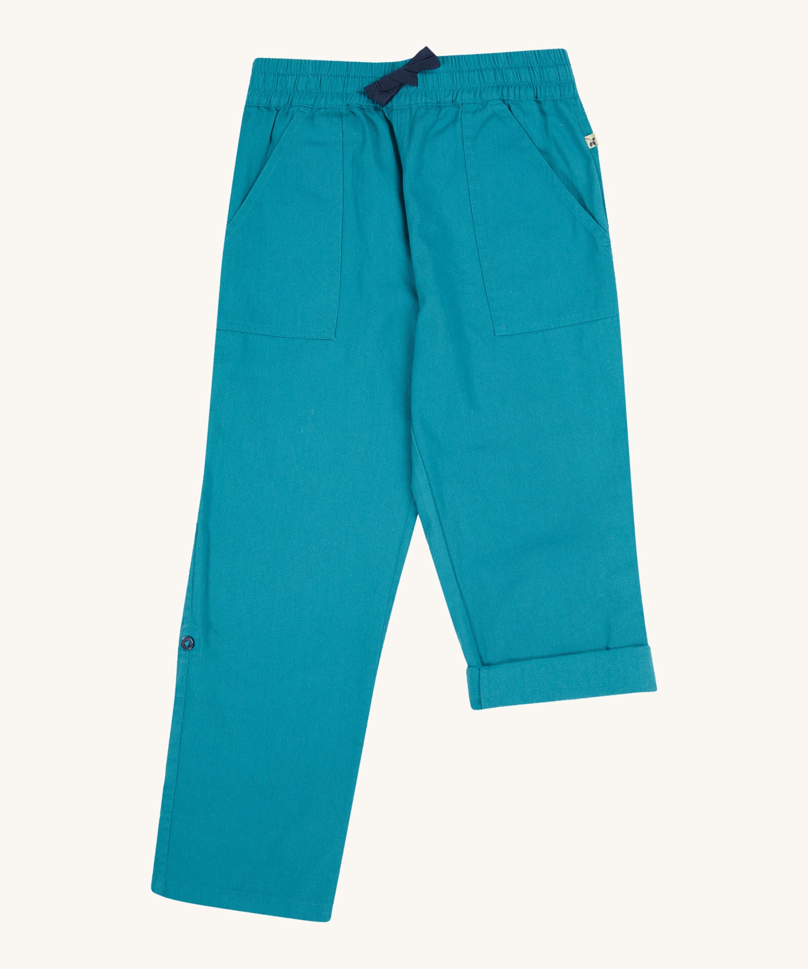 Frugi kids trousers in green, blue, turquoise colour on a cream background.