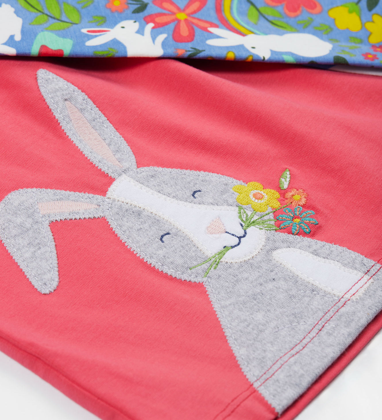 Close up of the Frugi kids watermelon iris bunny outfit. Showing the grey rabbit appliqué detail with light blue bottoms with white rabbits and floral prints on top on organic cotton fabric.