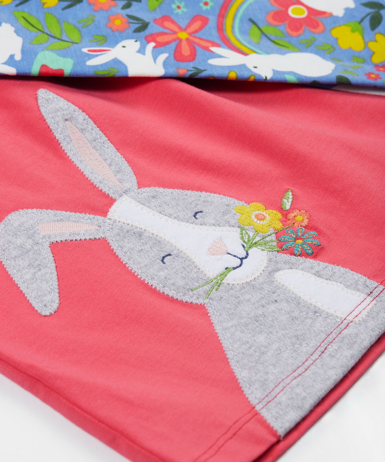 Close up of the Frugi kids watermelon iris bunny outfit. Showing the grey rabbit appliqué detail with light blue bottoms with white rabbits and floral prints on top on organic cotton fabric.