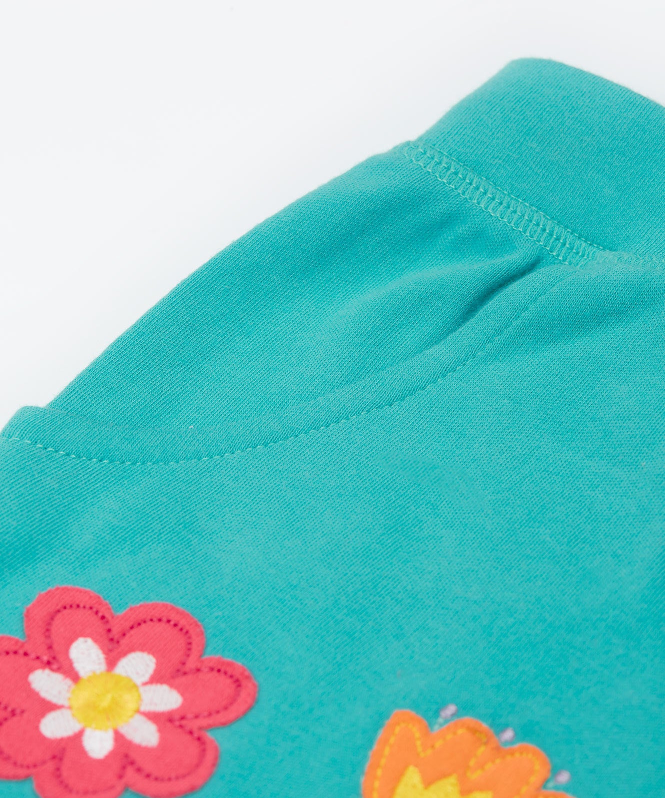 A close up of the shorts from the Frugi kids bee stripe outfit. Showing the pocket detail and flowers applique on a light blue organic cotton fabric