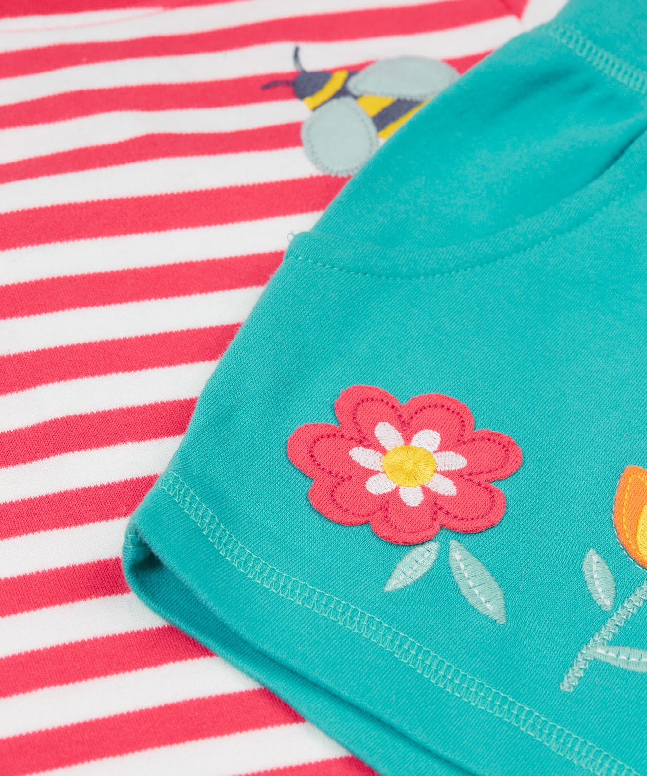 A close up of Frugi kids bee watermelon stripe outfit showing the bee and  flowers applique on a light blue, pink and white organic cotton fabric