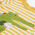 A close up of the Frugi kids wrap around crocodile outfit. Showing the front of the t shirt with crocodile eating a ice cream applique on yellow and white stripe organic cotton fabric