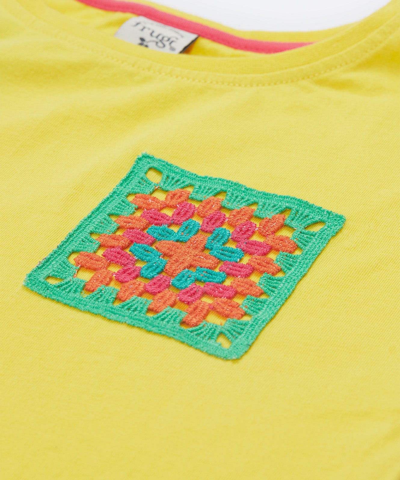 Close up of the Frugi kids yellow crochet pocket t-shirt. Showing the neck trim and the green, orange and blue crochet front pocket on yellow organic cotton fabric