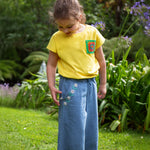 A child wearing the Frugi yellow Crochet Pocket T-Shirt with denim jeans