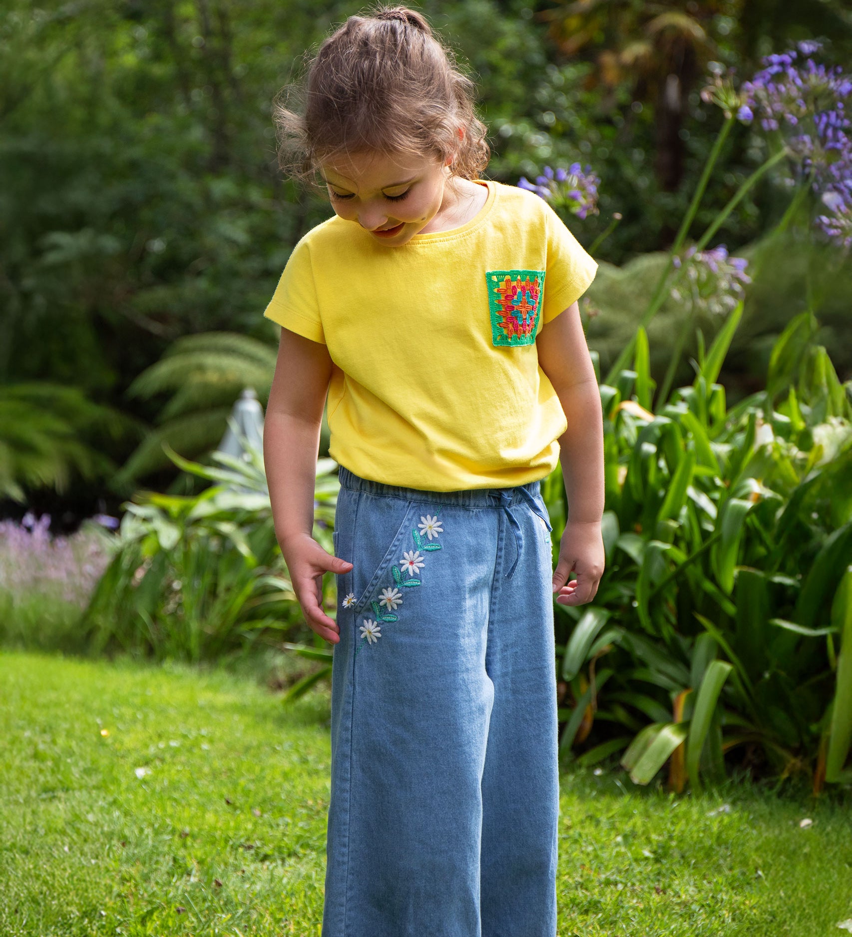 A child wearing the Frugi yellow Crochet Pocket T-Shirt with denim jeans