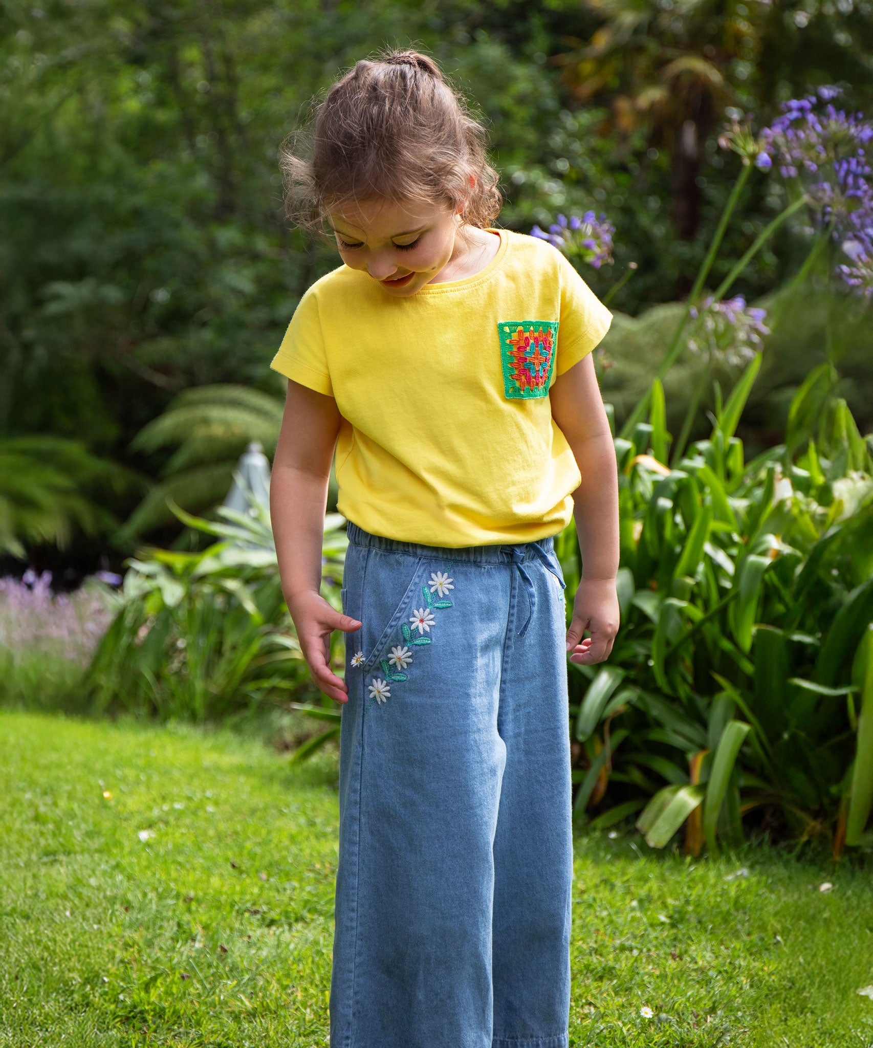 A child wearing the Frugi yellow Crochet Pocket T-Shirt with denim jeans