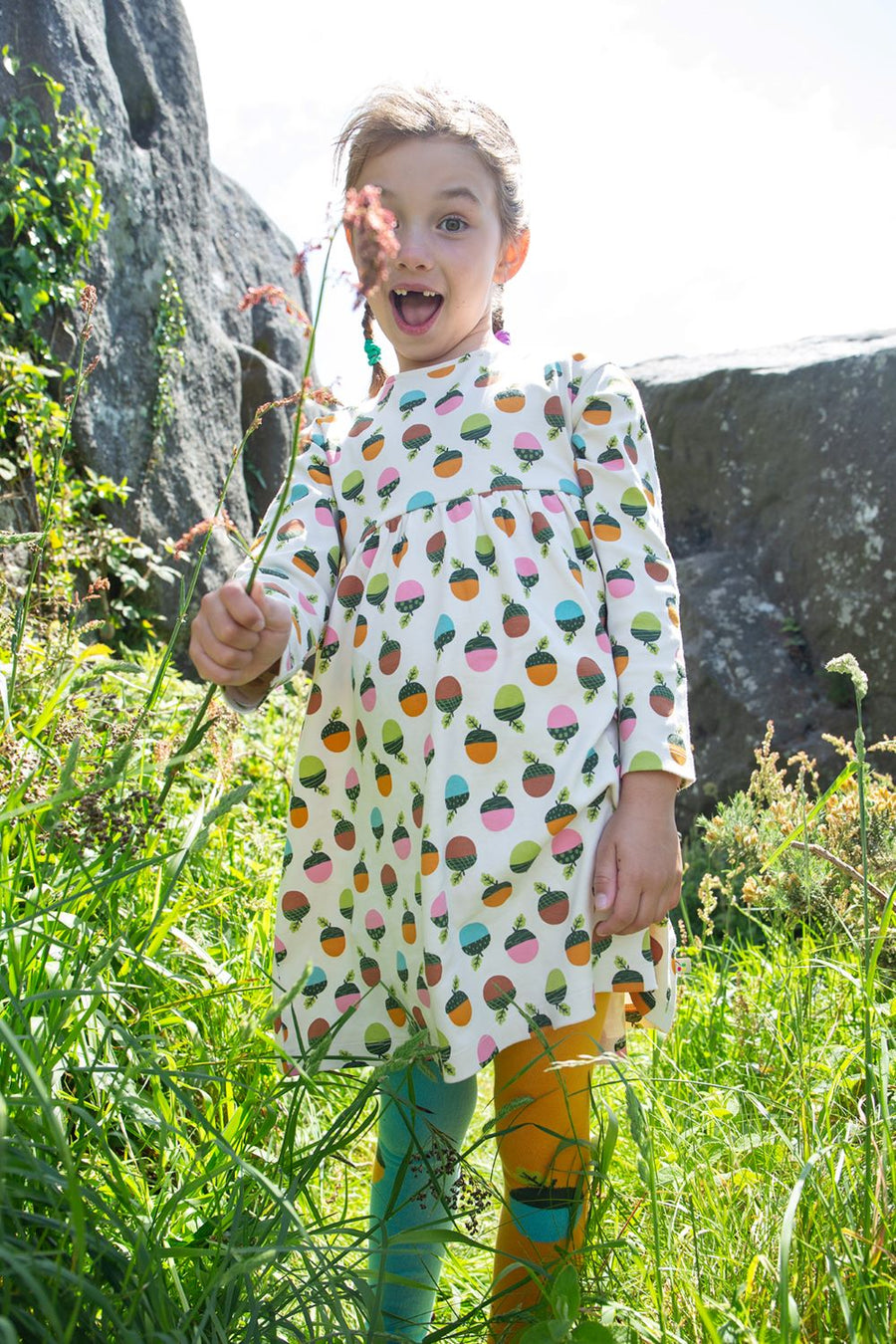 Child wearing Frugi Children's Bumblebee Acorn Organic Cotton Norah Tights outside on a grassy path with rocks behind.