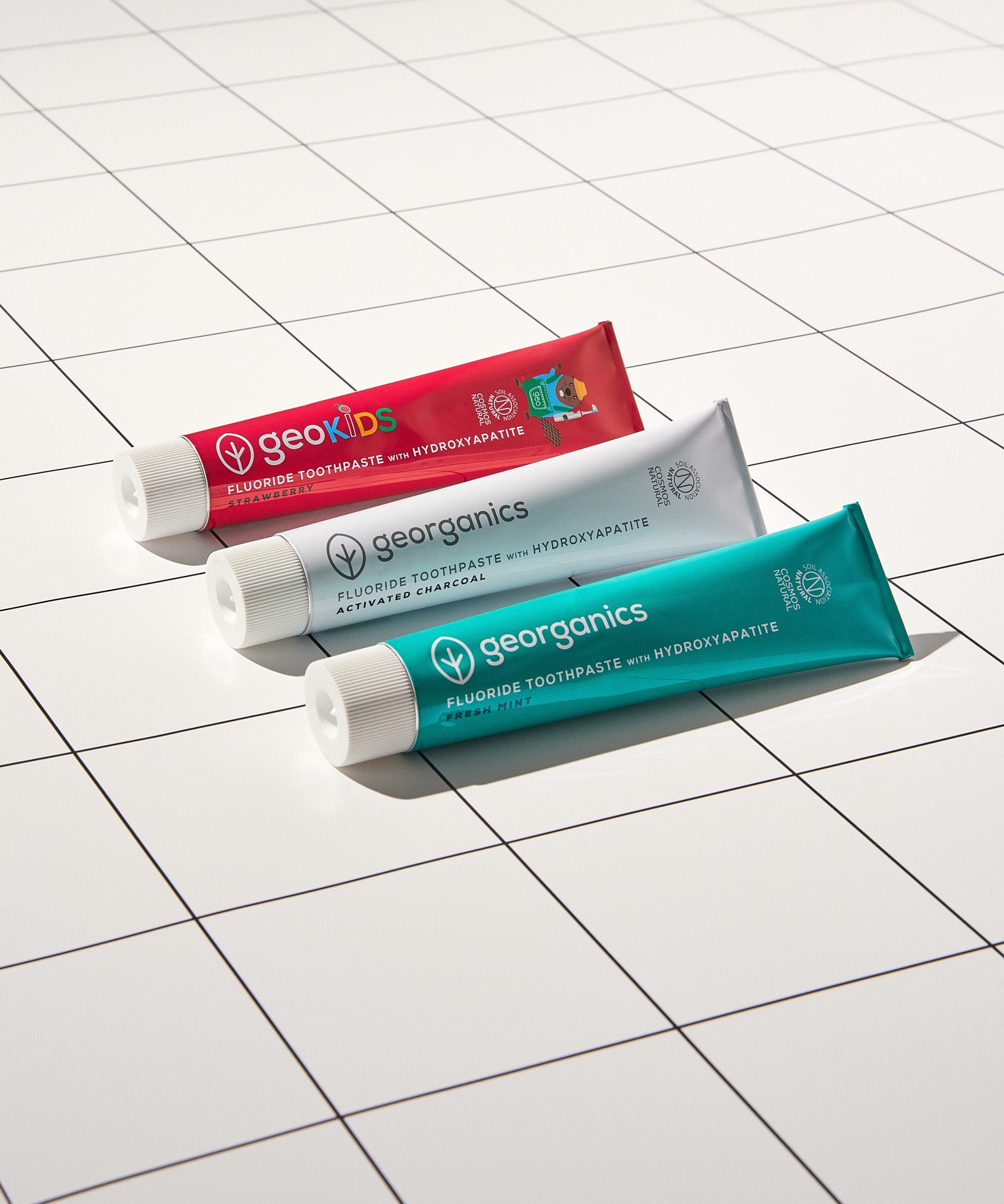 Georganics strawberry, activated charcoal and fresh mint toothpaste tubes on a white  and tile style floor. 