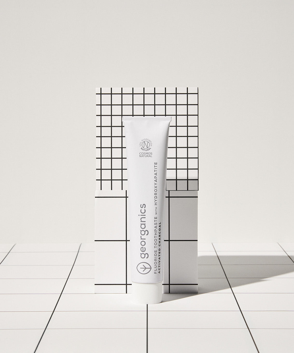 Front view of the Georganics activated charcoal hydroxyapatite toothpaste tube on a tile style floor and neutral background.