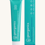 Front view of the Georganics fresh mint hydroxyapatite toothpaste. A light green tube with white and blue branding text next to matching cardboard packaging. 