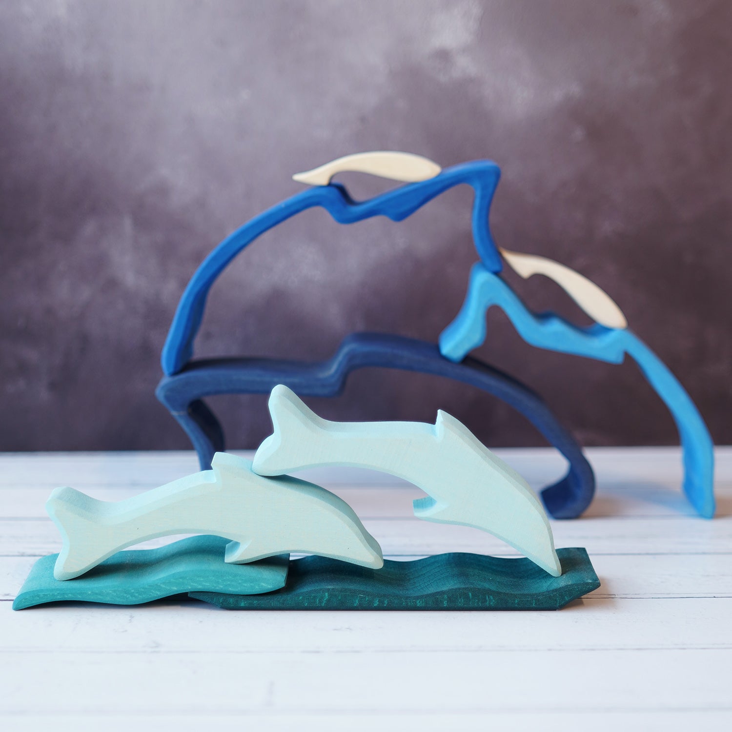 Wooden dolphin puzzle set in various shades of blue. The set includes a mixture of outlines and full-body shapes. In the background