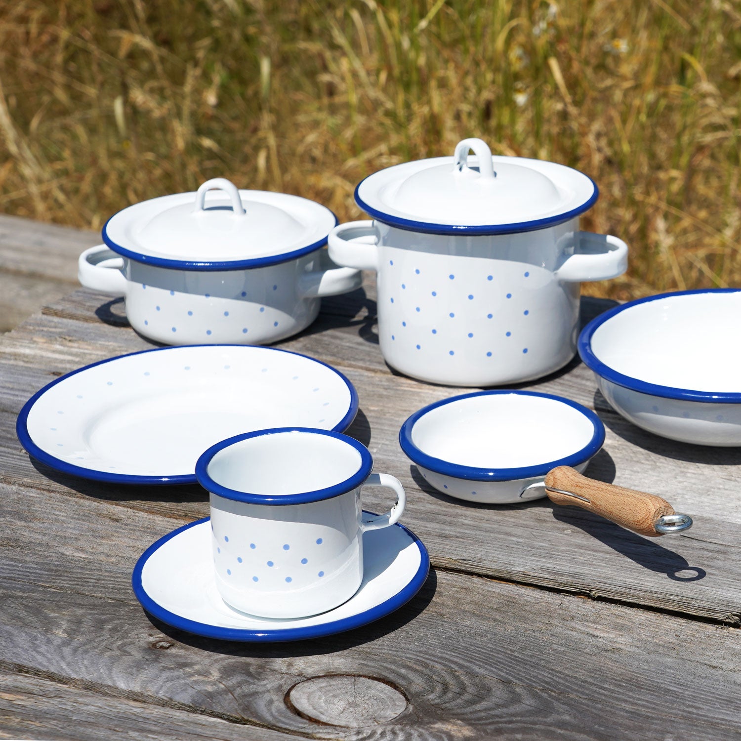 Glückskäfer Enamel Toy Cooking Pots pictured on a wooden bench outdoors