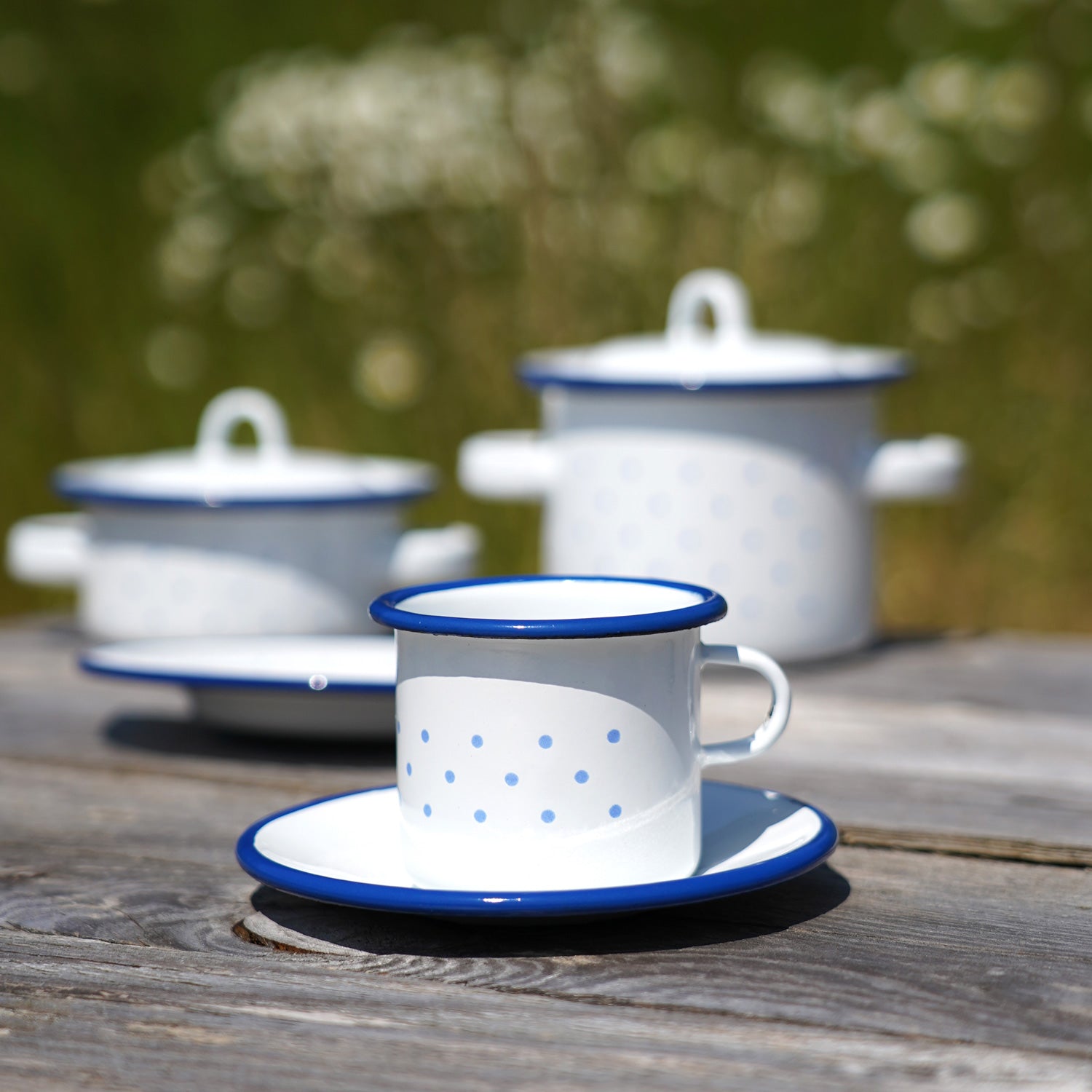 Glückskäfer Enamel Cup and Saucer pictured on a wooden surface with other enamel items seen in the background