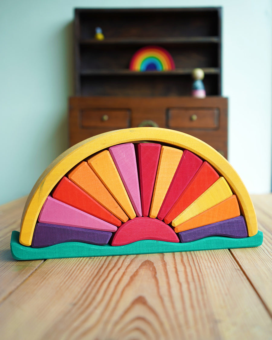 A Gluckskafer Yellow Sunray Arch pictured on a wooden surface. A dark wood miniature dresser can be seen in the background with a mini Grimm's rainbow placed on one of the shaves