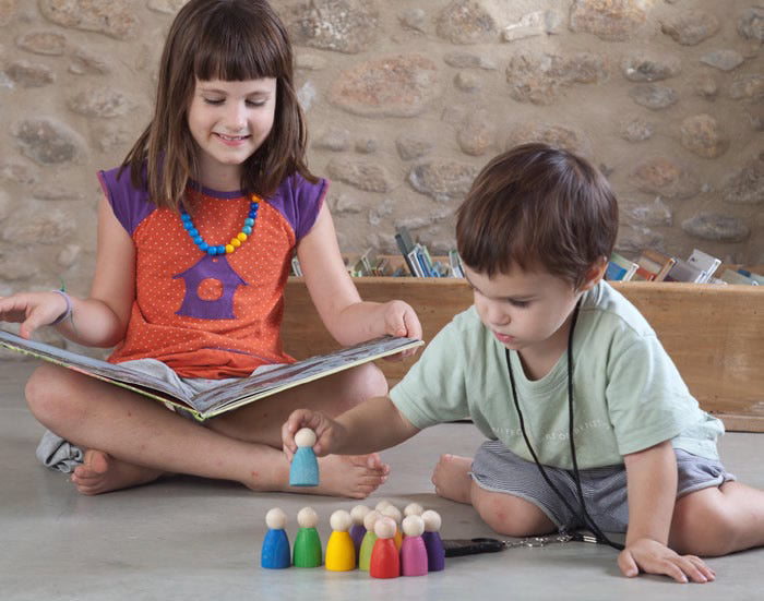 Grapat 12 Nins Wooden Peg Dolls in the colours of the rainbow being used for story telling. A classic Waldorf peg doll toy for open ended play. One child reading