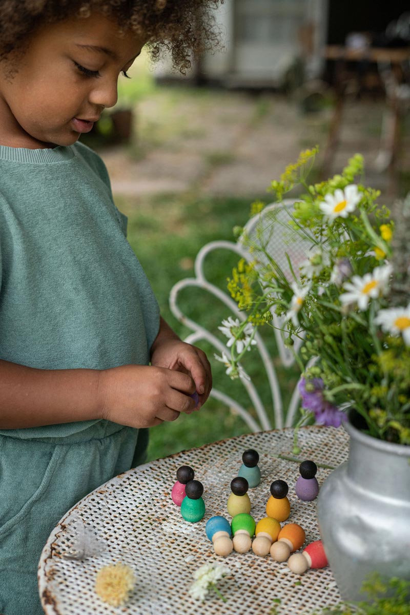 Close up of young child playing with the Grapat baby nin peg doll toys on a white metal table