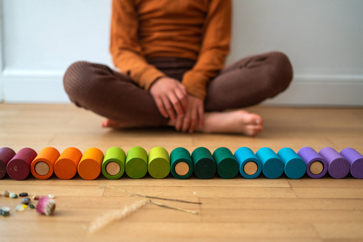 Close up of the Grapat rainbow wooden La toy tubes laid out in a row on a wooden floor