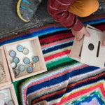 Close up of child crouched down next to some Grapat wooden boxes filled with bottle tops and paper shapes