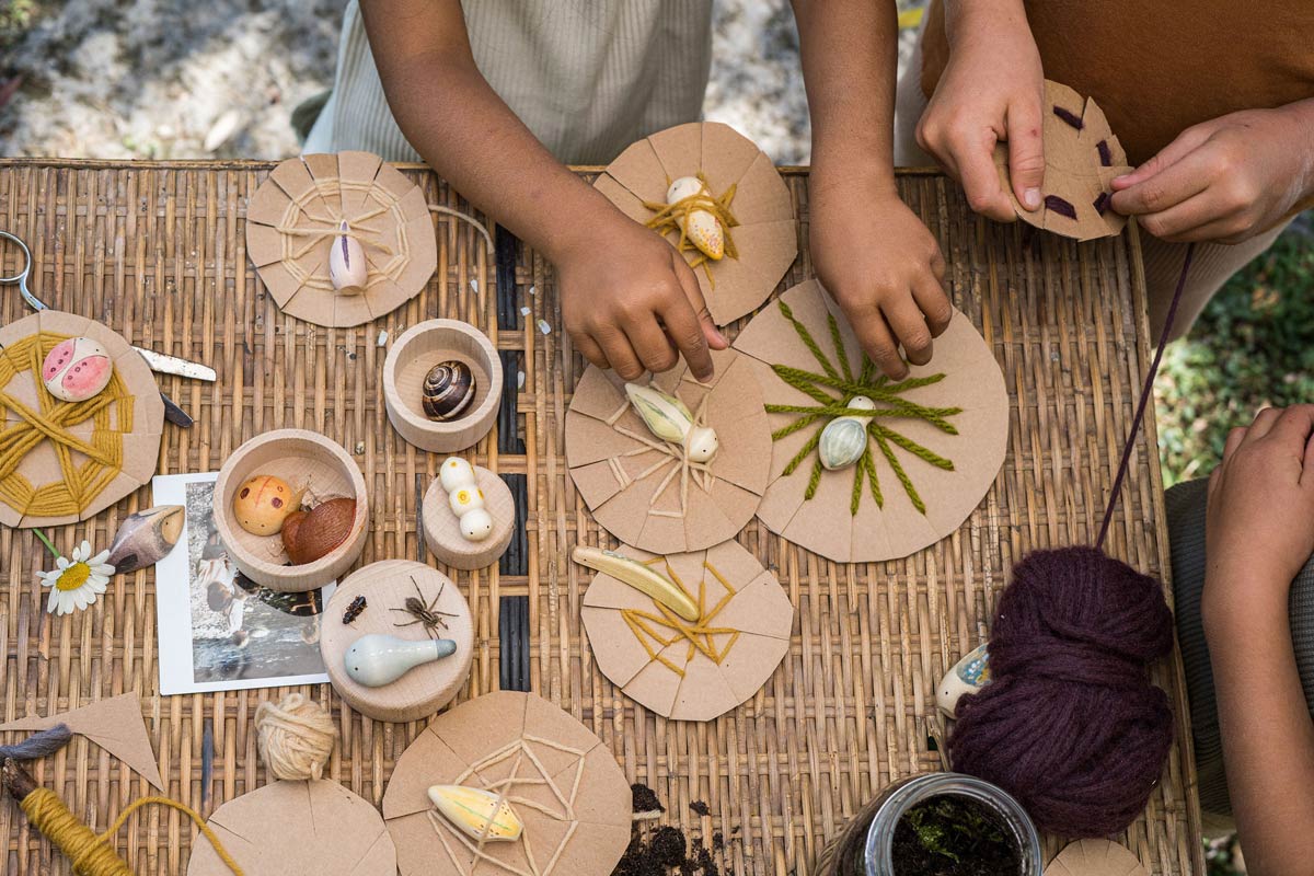 Close up of childrens hands doing crafts with the Grapat plastic-free wooden wild creature toys on a woven table