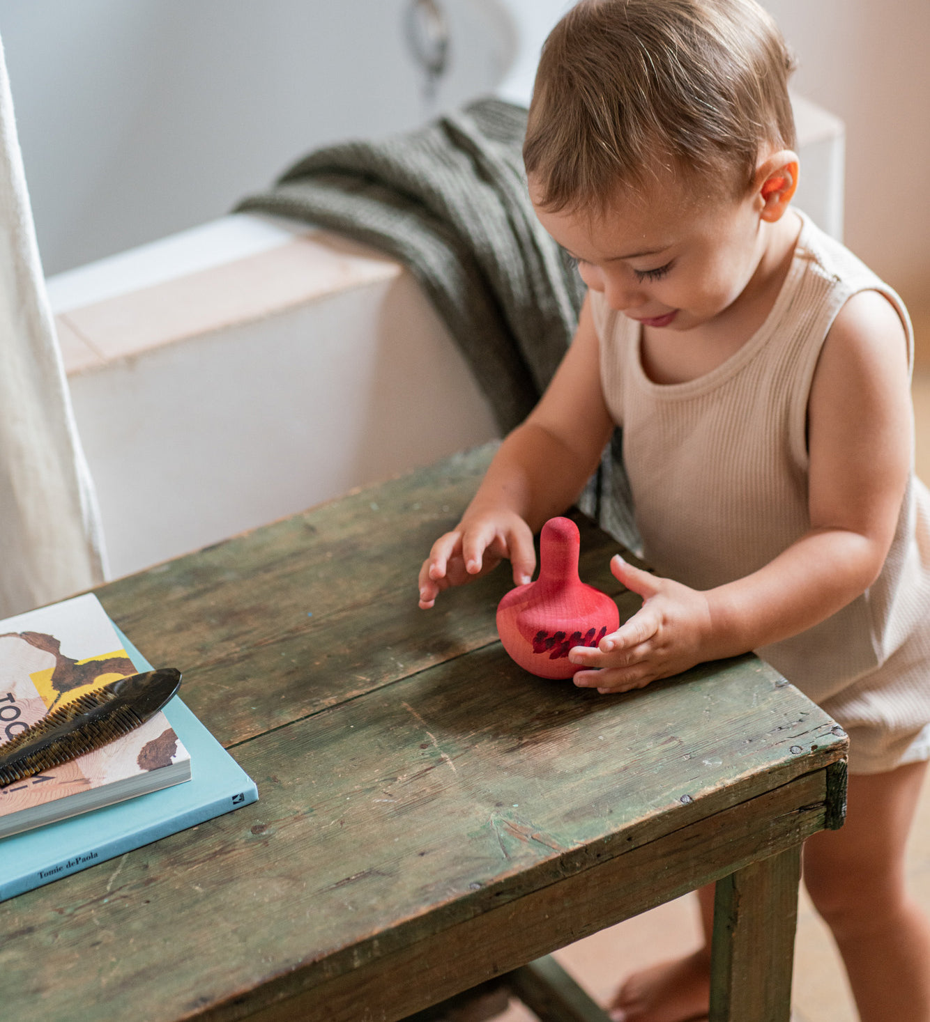 Child playing in the bathroom next to a wooden table with the Grapat wooden pink chill wobbly bird resting on top on the wooden table