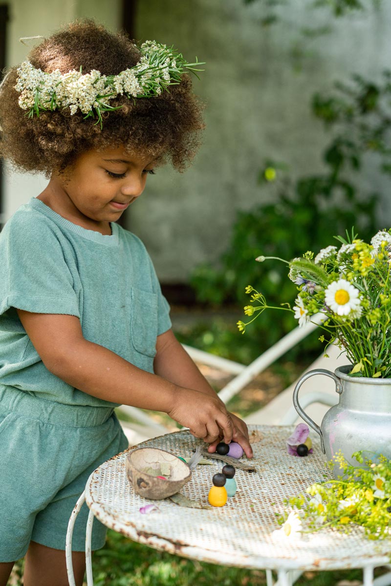 Close up of child playing with the eco-friendly Grapat baby nin toys on a white table next to a metal jug of flowers