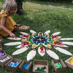 Young girl laying out Grapat mandala toy pieces on the plastic-free petal blocks on some green grass