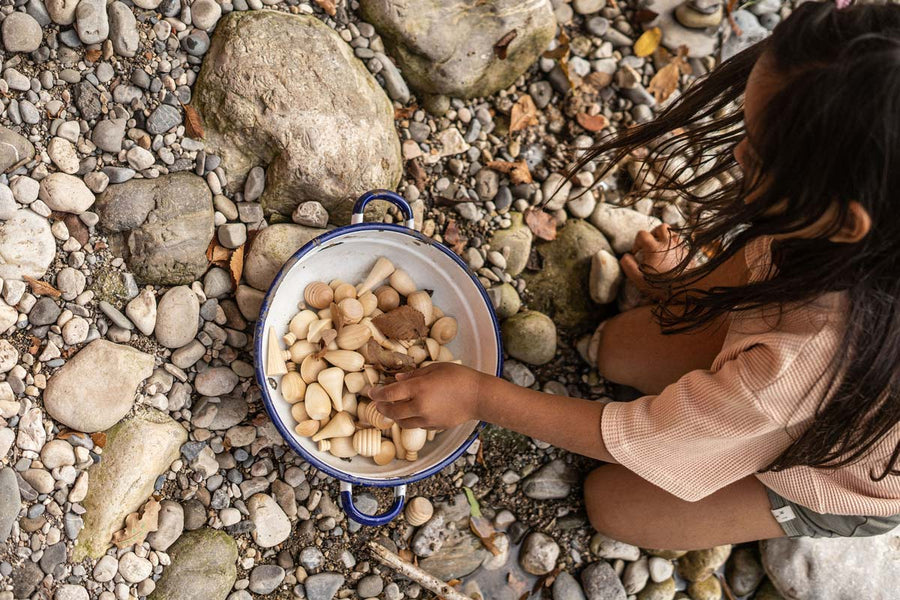 Close up of a child playing with the Grapat plastic-free wooden mandala pieces in a white bowl on some small rocks