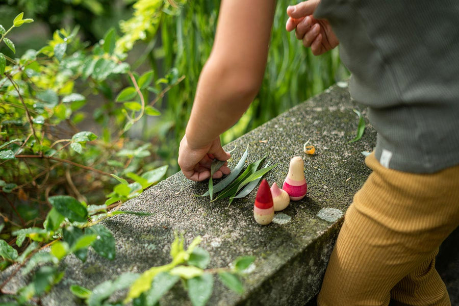 Close up of child playing with the Grapat yay wooden figures on a stone wall next to some green leaves