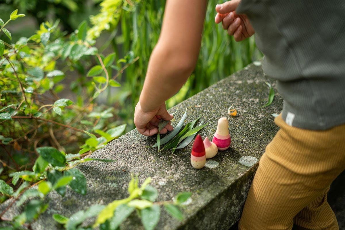 Close up of child playing with the Grapat yay wooden figures on a stone wall next to some green leaves