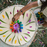 Close up of a girl lining up Grapat eco-friendly wooden rainbow mandala mushrooms in a circle on a wooden board