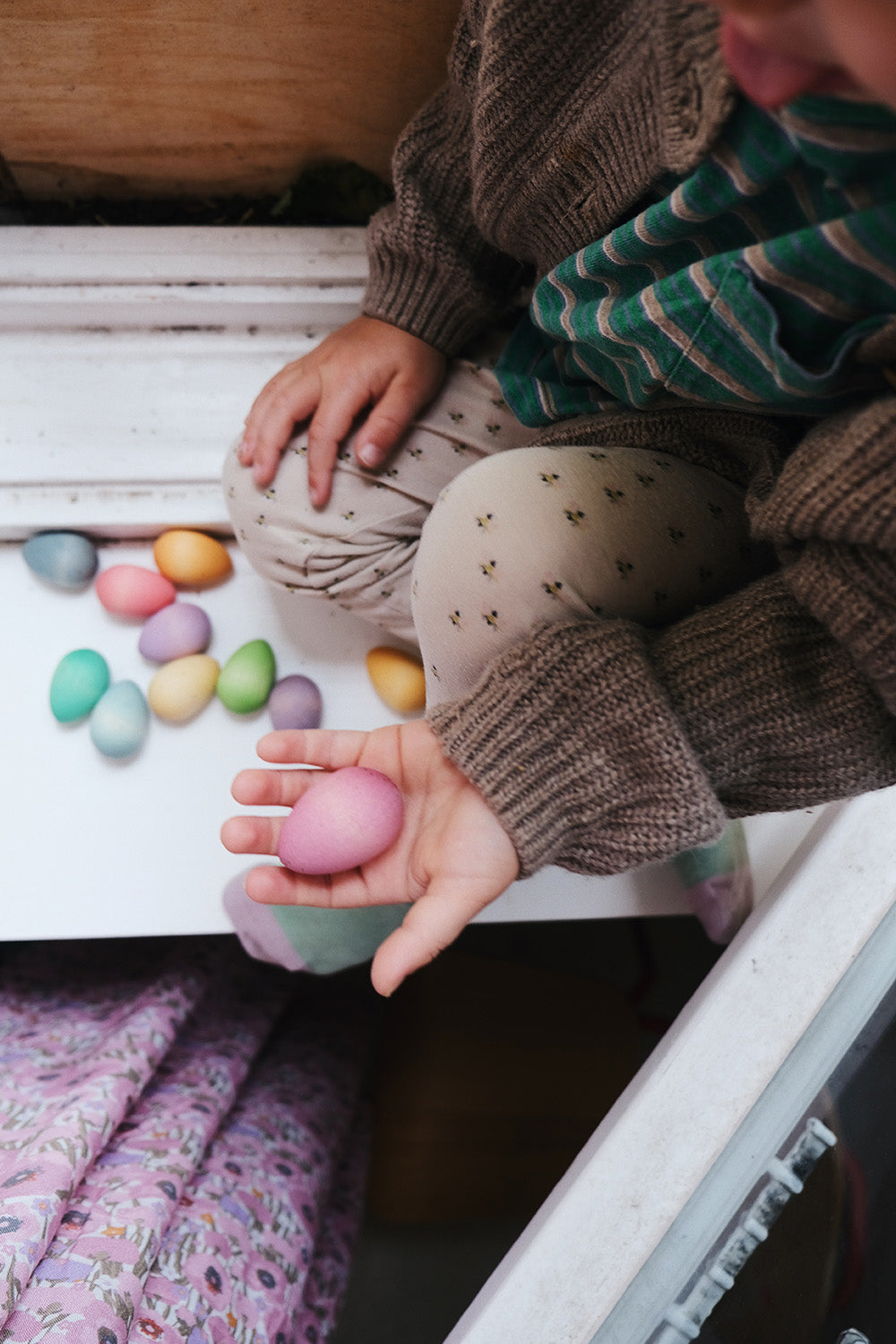 a child holding pink grapat wooden egg