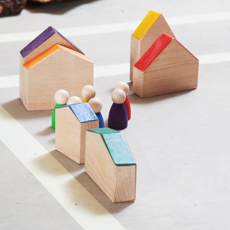 Grapat Six Wooden Houses Set in different simple geometric shapes in natural wood and colourful painted roofs. Displayed in a village scene with a collection of colourful peg people in the centre. White background.