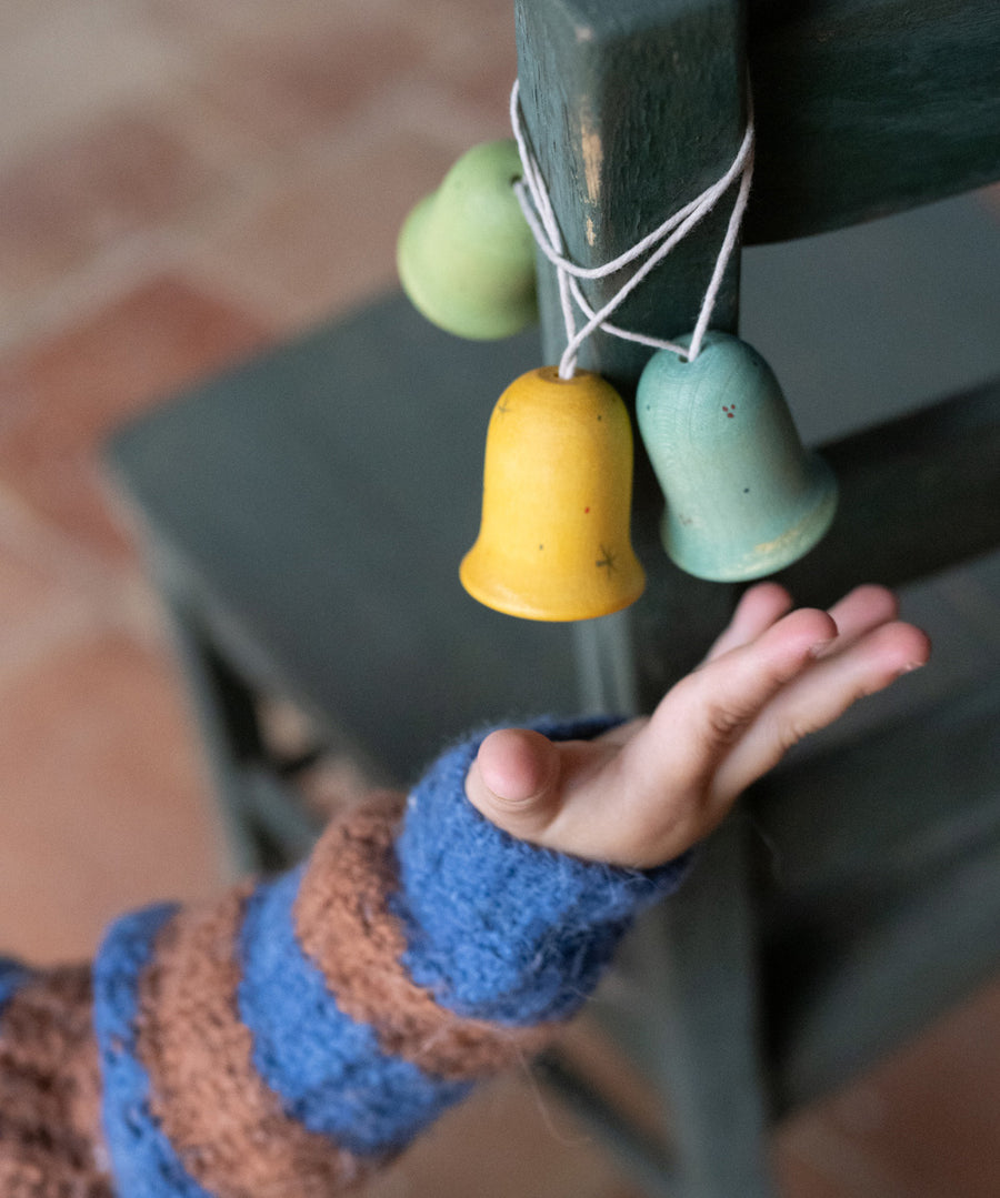 A light blue, yellow and green Grapat wooden jingle joy bells hanging on a chair