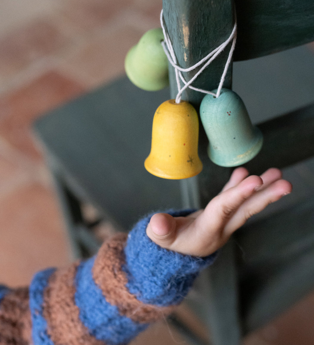 A light blue, yellow and green Grapat wooden jingle joy bells hanging on a chair