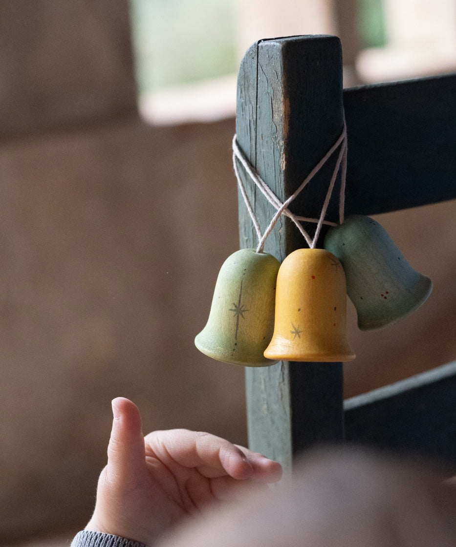 A close up of the light blue, yellow and green Grapat wooden jingle joy bells hanging on a chair