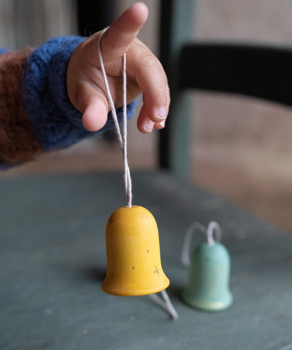 A close up of the yellow wooden Grapat jingle joy bells hanging on a child's finger