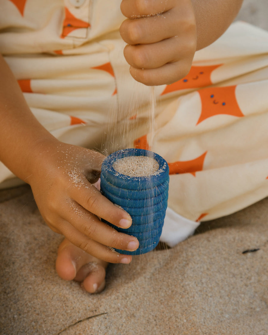 A child is playing with the yellow vase and orange pot from the Grapat Wooden Rainbow Sorting Pots