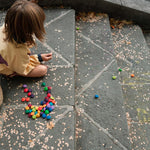 Child crouched down on some stone stairs playing with Grapat wooden rainbow mandala flowers