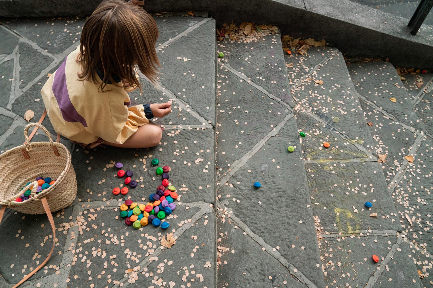 Child crouched down on some stone stairs playing with Grapat wooden rainbow mandala flowers