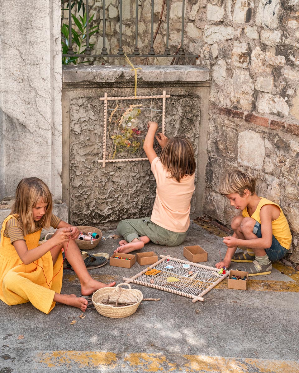 Close up of the Grapat wooden weaving frame on the floor next to a child's leg