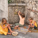 Close up of the Grapat wooden weaving frame on the floor next to a child's leg