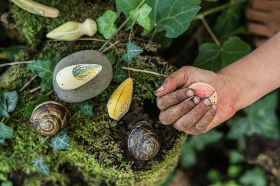 Close up of a childs hand holding a Grapat eco-friendly wooden wild creature toy above some dark green leaves