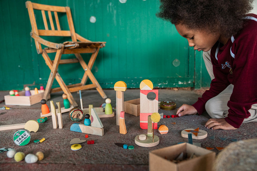 Child kneeling down playing with toy blocks from the Grapat wooden happy place set