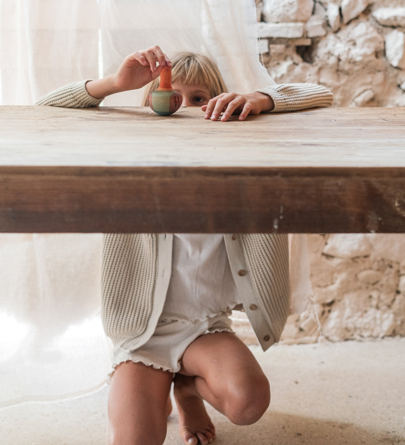 Child playing with the Grapat wooden mellow orange wobble wooden bird on a wooden table showing the hand painted pink and purple detailing. 